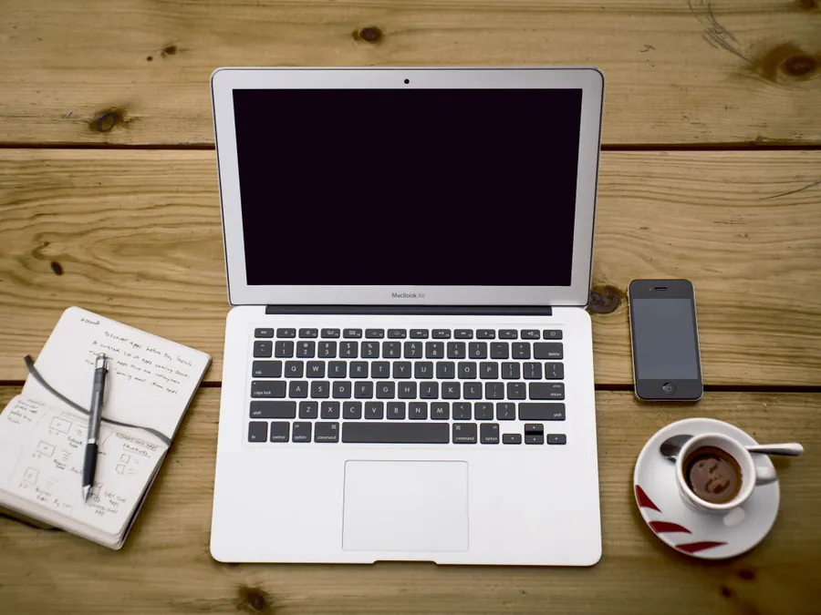 A laptop, open notebook and coffee cup arranged on a wooden desk